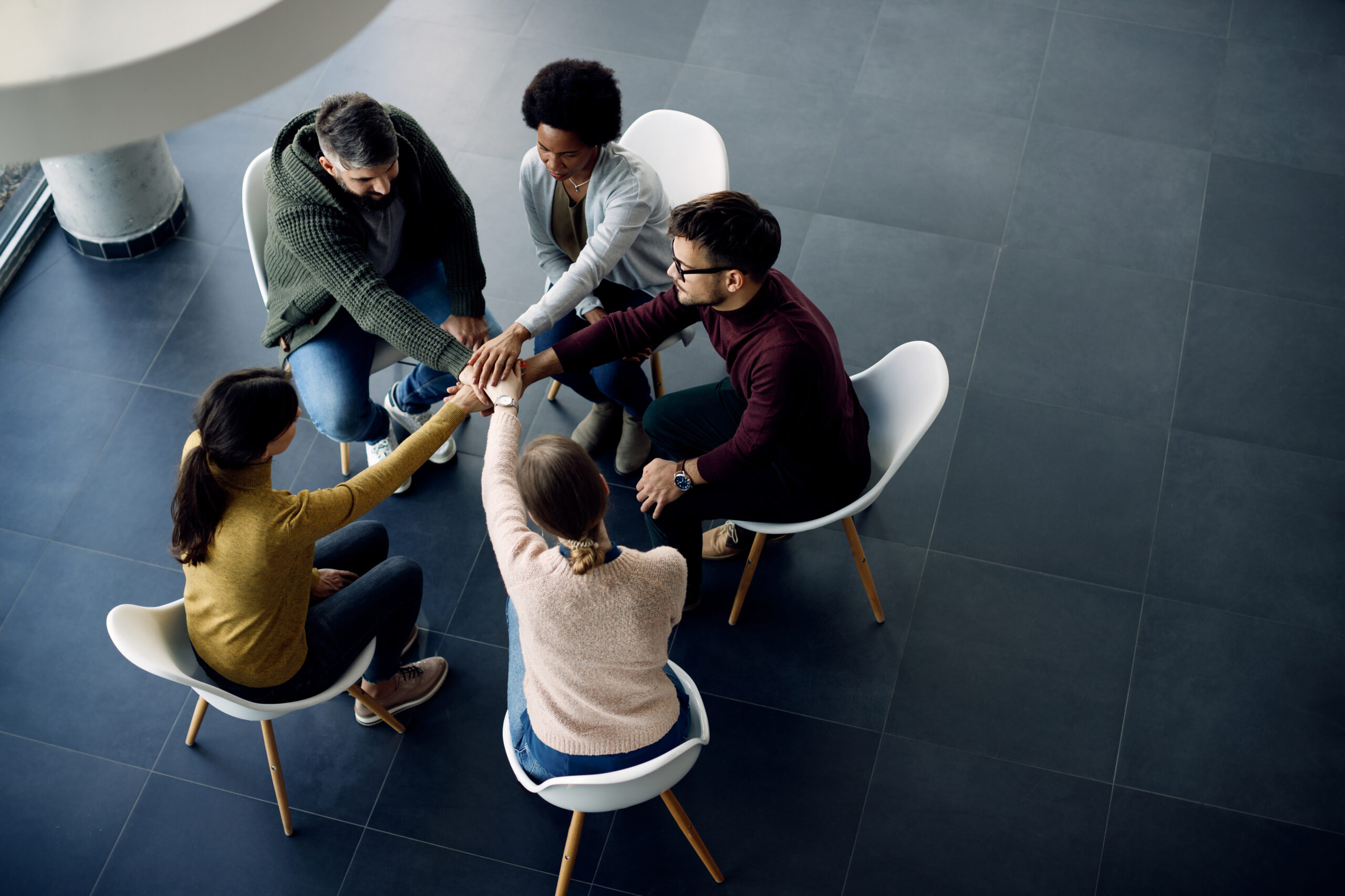 Above view of group therapy participants holding hands in unity